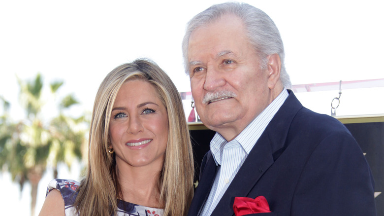 Jennifer Aniston wearing a floral dress and John Aniston wearing a blue jacket and white striped collared shirt