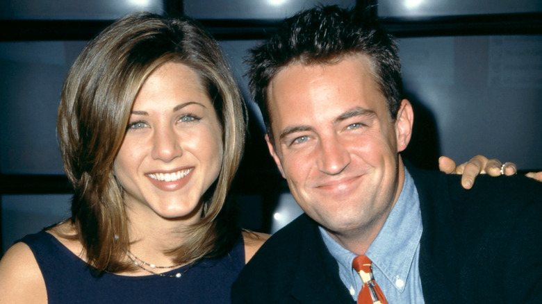 Jennifer Aniston in a blue dress and Matthew Perry in a black jacket, blue collared shirt, and colorful tie