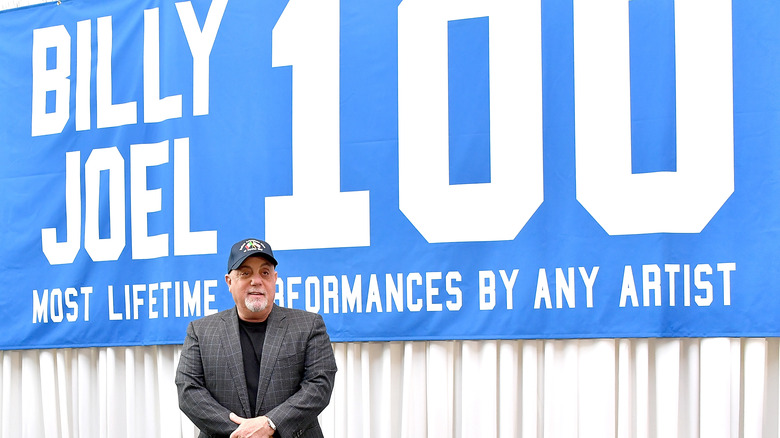 Billy Joel stands in front of "Billy Joel 100" banner