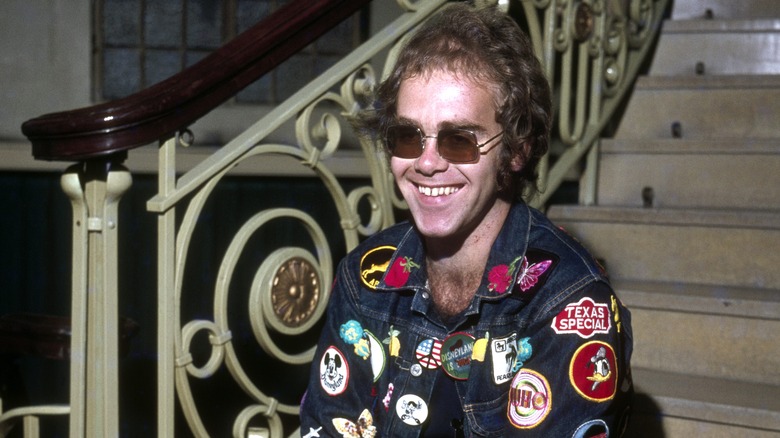 Elton John smiling and sitting on steps