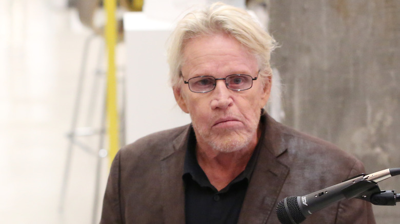 Gary Busey speaking into a microphone with glasses