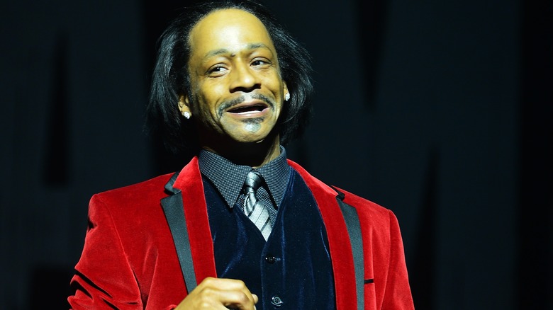 Katt Williams speaking on stage in red blazer