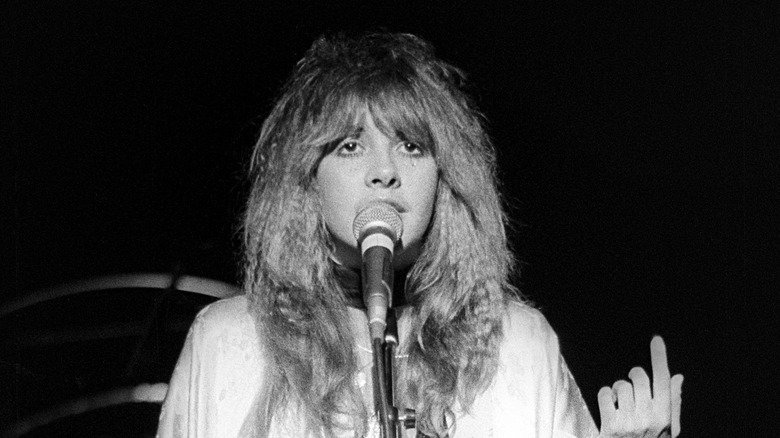 Stevie Nicks wearing a white shawl while singing