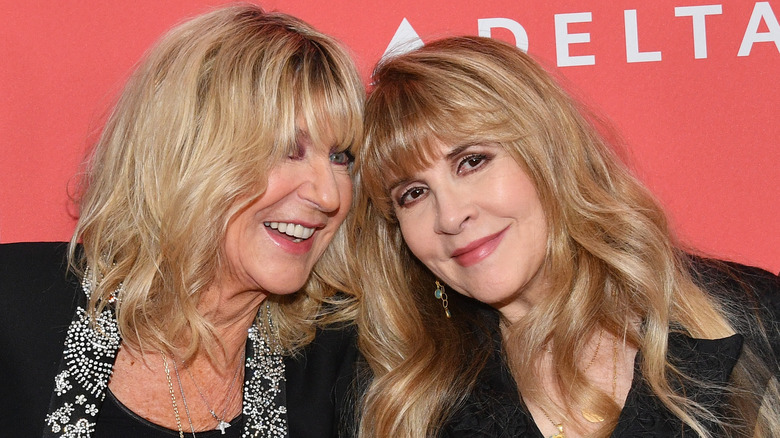 Christine McVie wearing a black jacket with silver embellished trim and Stevie Nicks wearing a black jacket and gold and green earrings