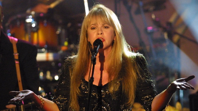 Stevie Nicks wearing a black and gold lace dress with gold bracelets