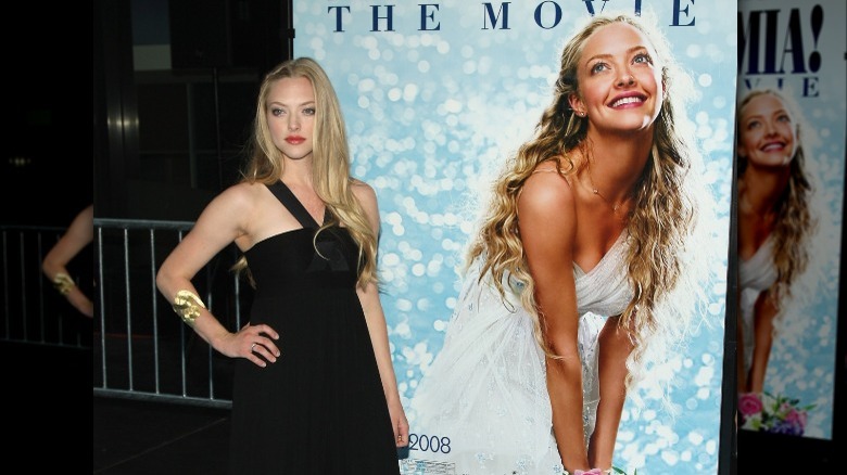 Amanda Seyfried standing with Mamma Mia poster