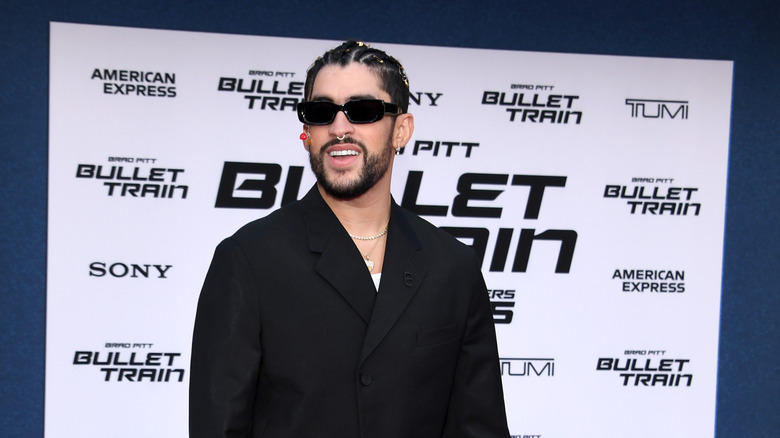 Bad Bunny in a black shirt and black sunglasses posing in front of a step-and-repeat for "Bullet Train"