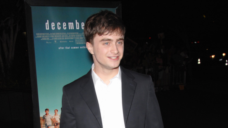 Daniel Radcliffe poses in dark jacket and white shirt.