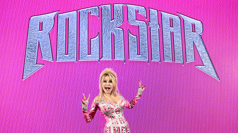 Dolly Parton poses with her mouth open and holding peace sign in front of pink Rockstar banner