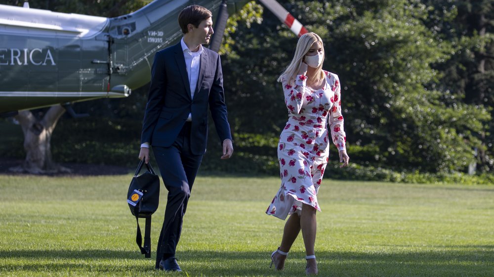 Jared Kushner in a blue suit, Ivanka Trump in a white floral dress and face mask, walking outside