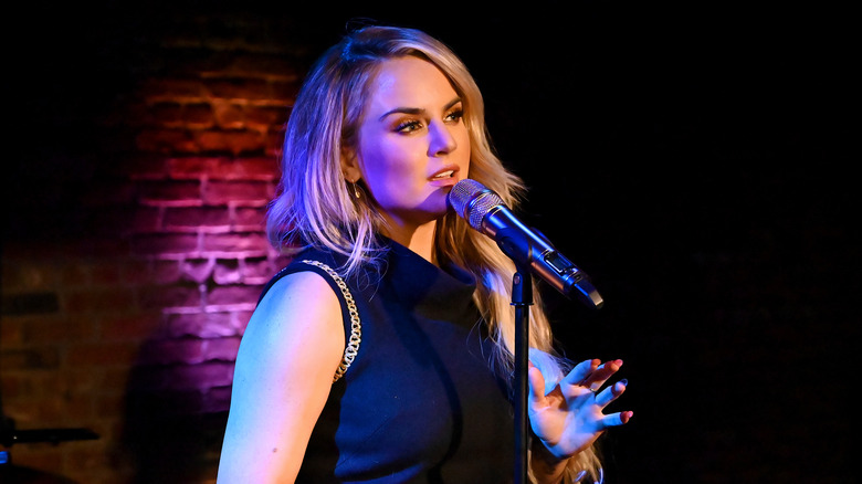 Joanna Levesque wearing a black sleeveless dress while singing into a microphone