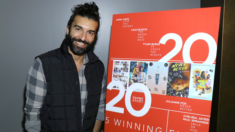 Justin Baldoni smiling next to a poster