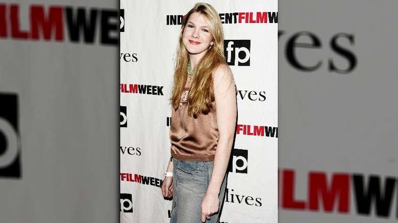 lily rabe smiling in a silk vest and denim skirt