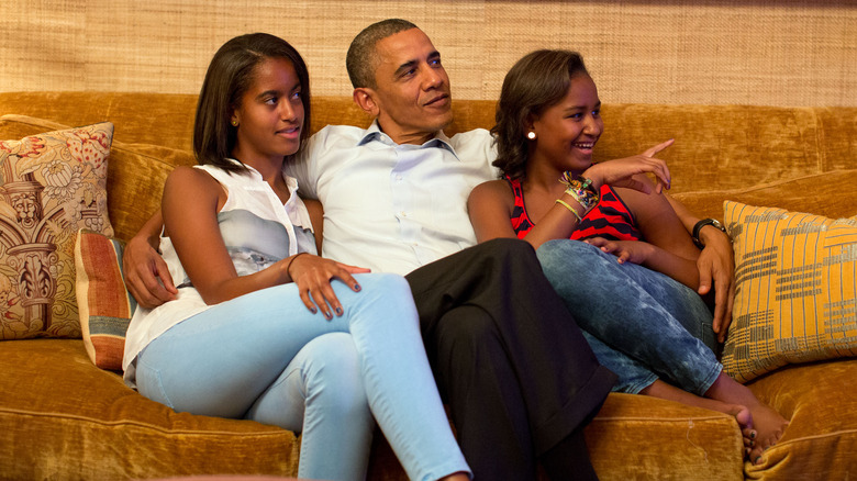 Malia and Sasha sitting on a couch with Barack Obama