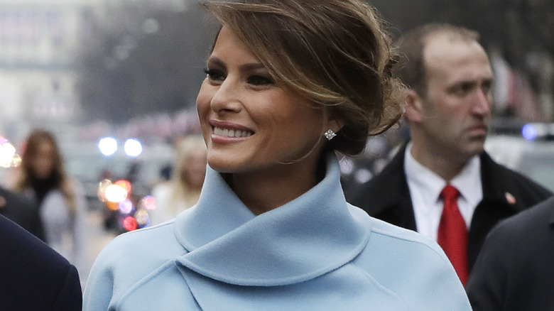 Melania Trump laughing, light blue coat, hair in updo