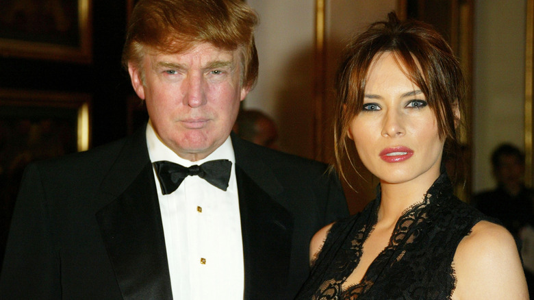 Melania Trump pouting next to Donald in the early 2000s, wearing black dress ensemble with updo