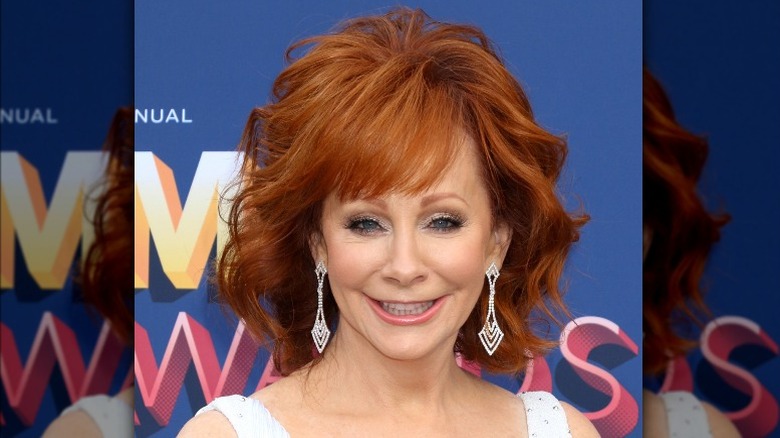 Reba McEntire smiling, wearing big earrings