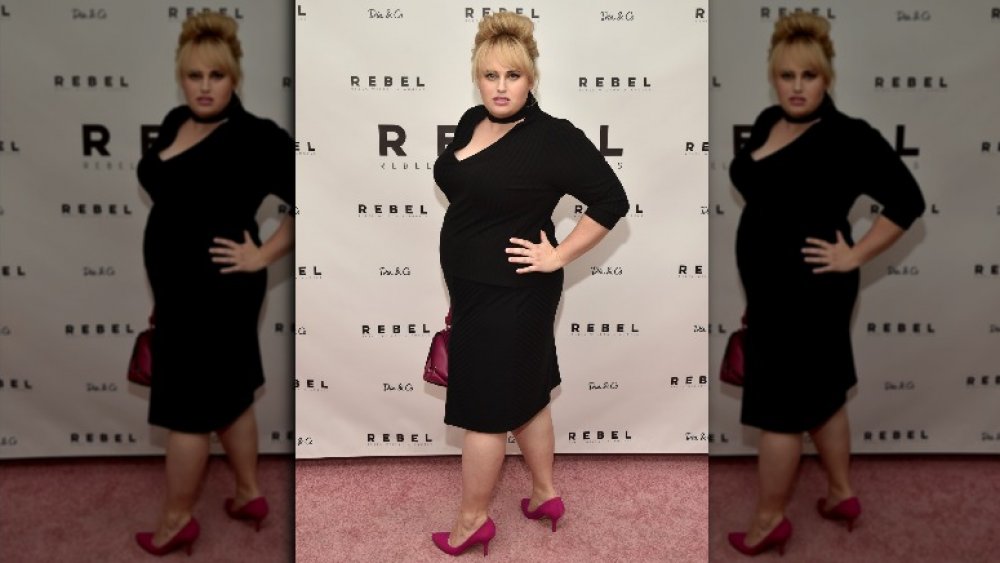 Rebel Wilson modeling a black dress for her fashion line 