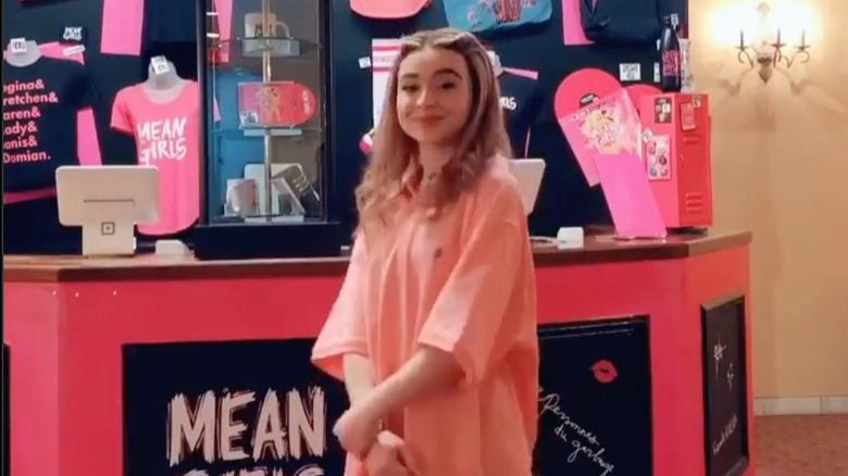 Sabrina Carpenter in costume as Cady Heron from Mean Girls wearing a large pink polo shirt and blonde wig