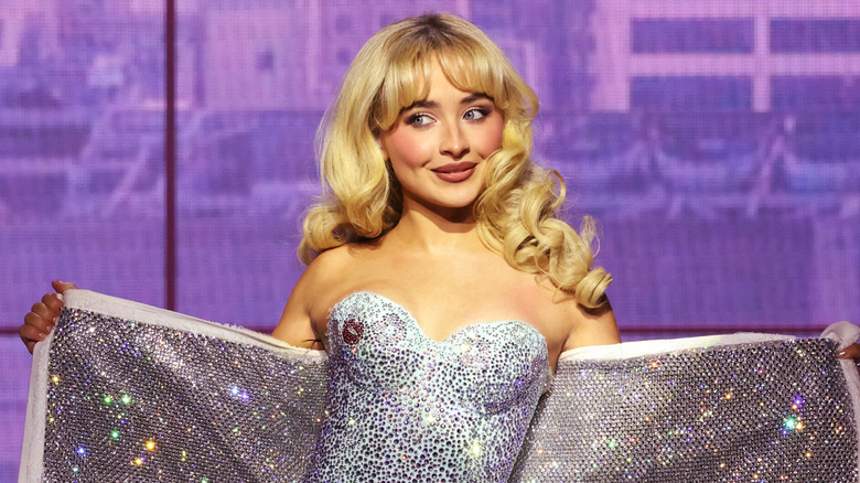 Sabrina Carpenter with long blonde curled hair wearing a sequined corset holding a sequined towel