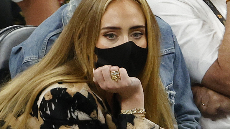 Adele sitting at a basketball game wearing a black face mask