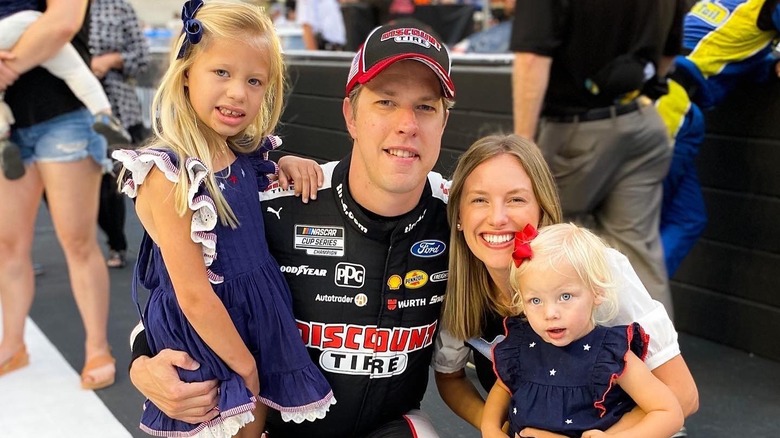 Brad Keselowski and wife Paige White crouched down and smiling with daughters Scarlett and Autumn