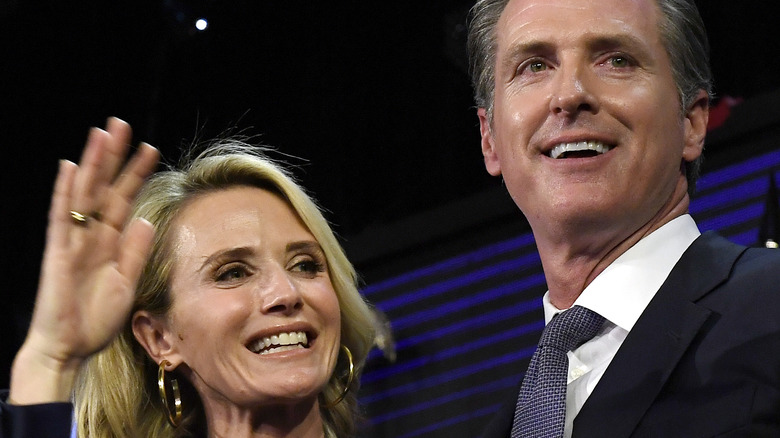 Jennifer Siebel and Gavin Newsom smiling and waving