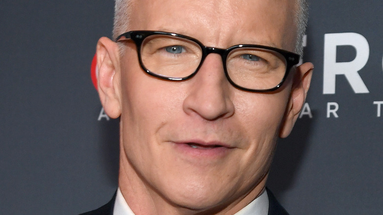 Anderson Cooper smiles in black frame glasses.
