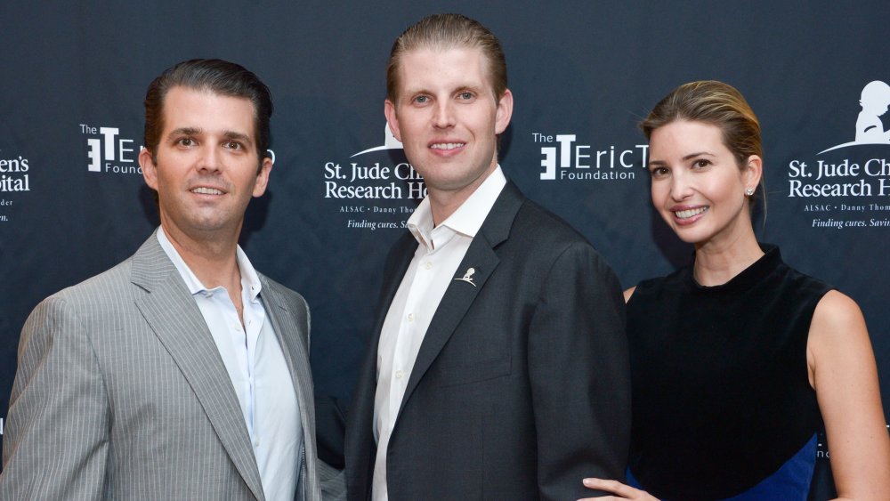 Donald Trump Jr., Eric Trump, and Ivanka Trump posing in front of wall