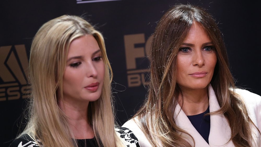 Ivanka Trump in black dress, Melania Trump in a white coat, both looking serious