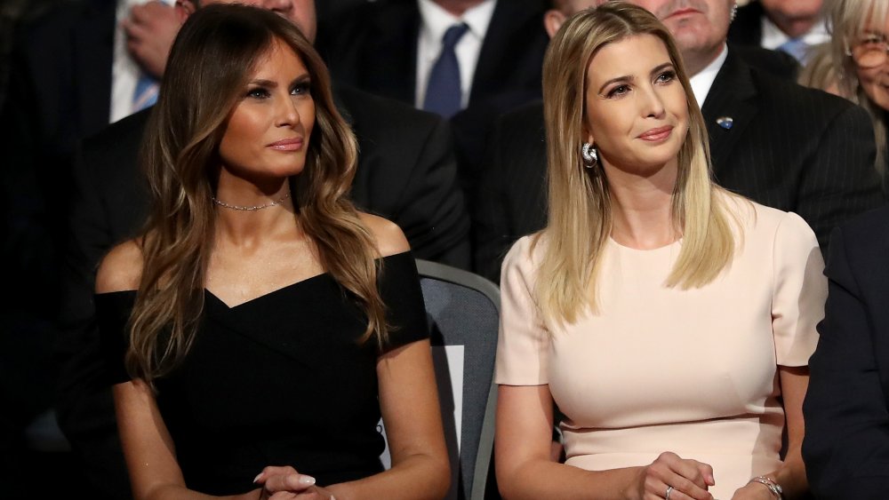 Melania Trump, in a black dress, sitting next to Ivanka Trump, in a light pink dress, both with soft smiles