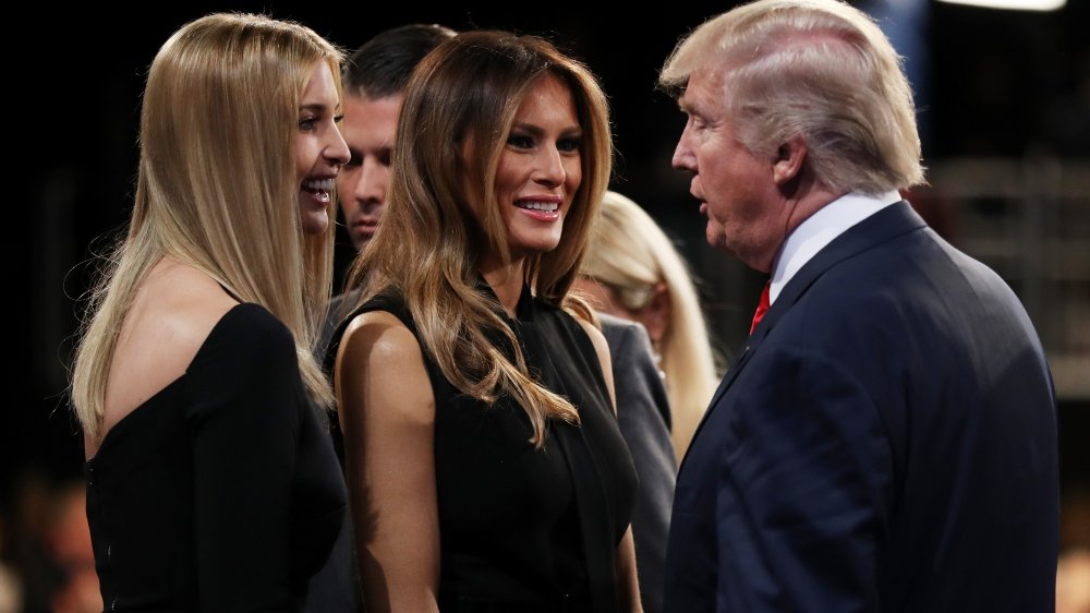 Ivanka Trump and Melania Trump, both wearing black dresses, smiling at Donald Trump