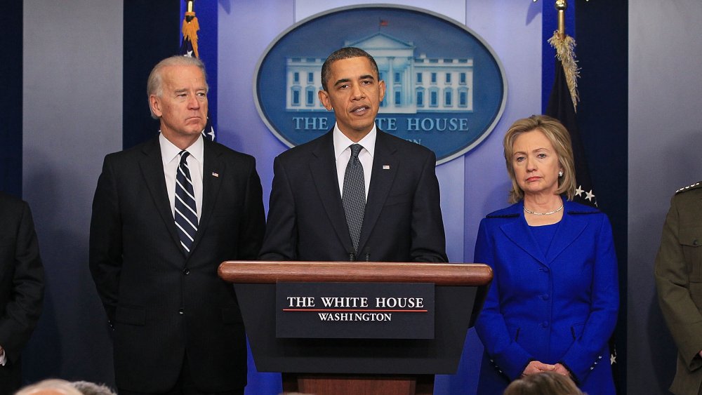 Barack Obama giving a speech, with Joe Biden and Hillary Clinton standing at either side