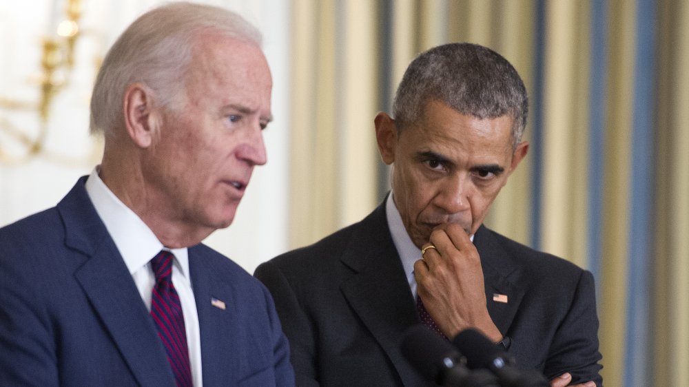 Joe Biden speaking, Barack Obama behind him, listening