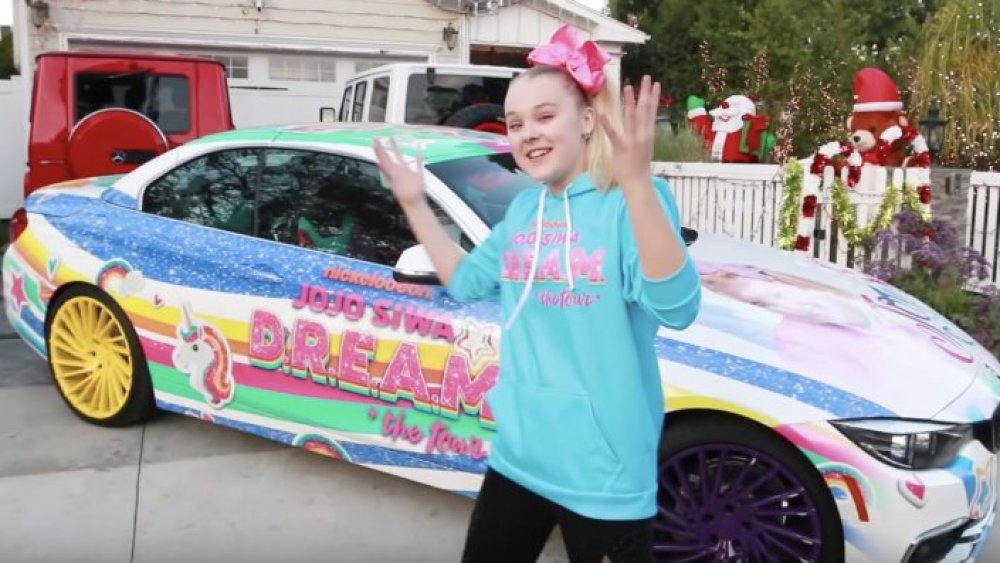 JoJo Siwa talking animatedly in front of her car