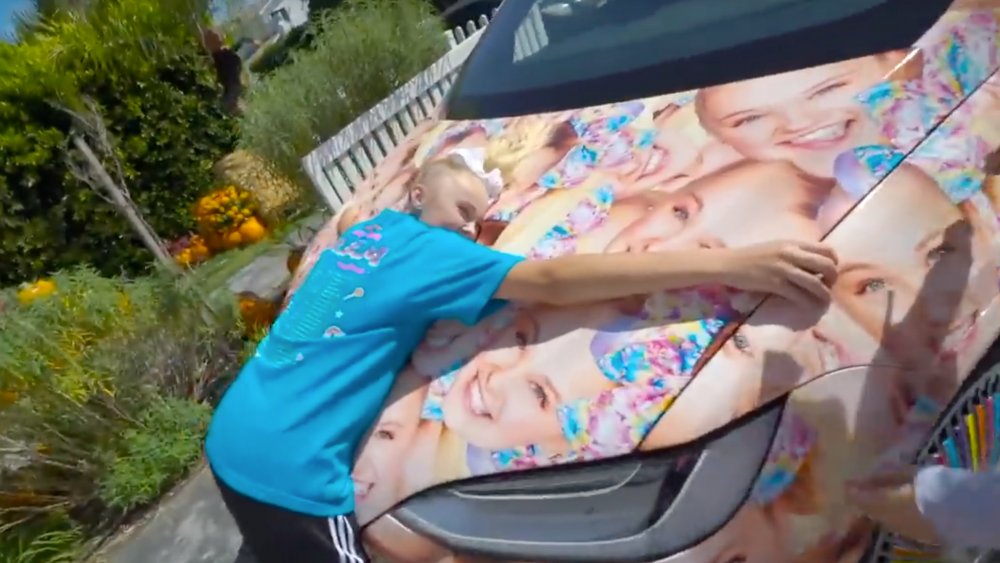 JoJo Siwa hugging the hood of her custom Tesla