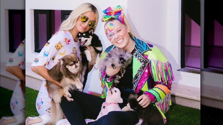 Paris Hilton and JoJo Siwa smiling together while holding dogs