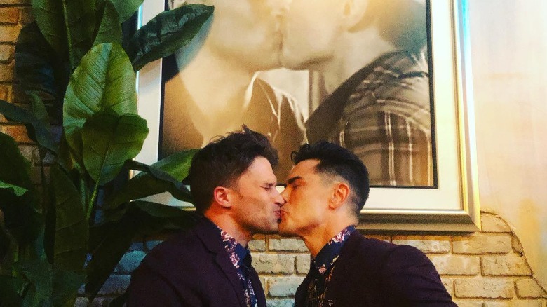 Tom Schwartz kissing Tom Sandoval below a photo of them kissing