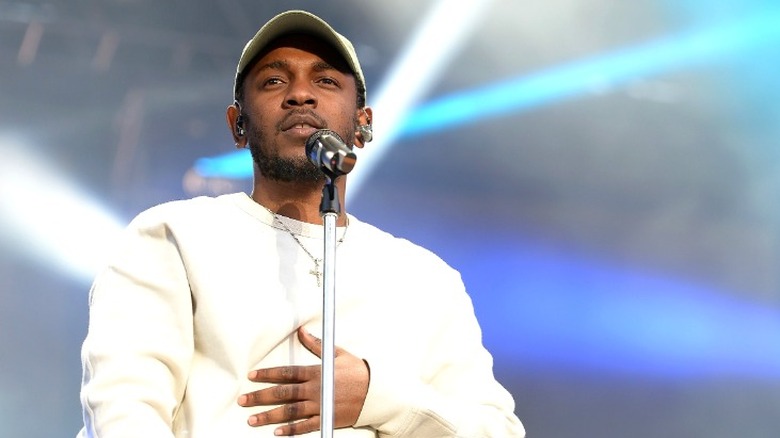 Kendrick Lamar speaking at microphone wearing white sweatshirt