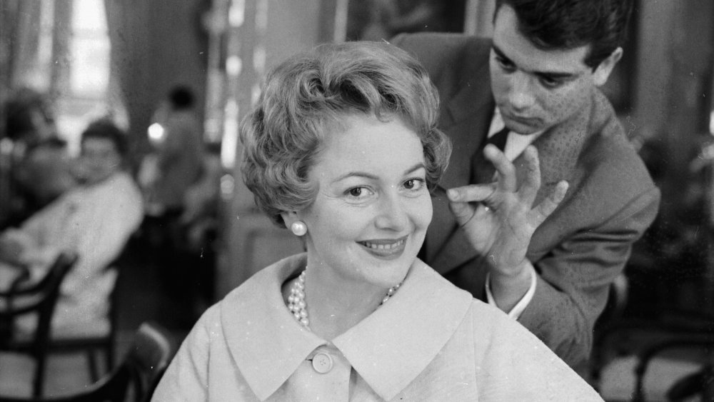 Black-and-white photo of Olivia de Havilland smiling while getting her hair done