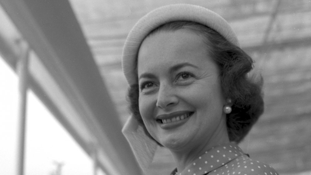 Black-and-white photo of Olivia de Havilland wearing a hat and pearl earrings, smiling