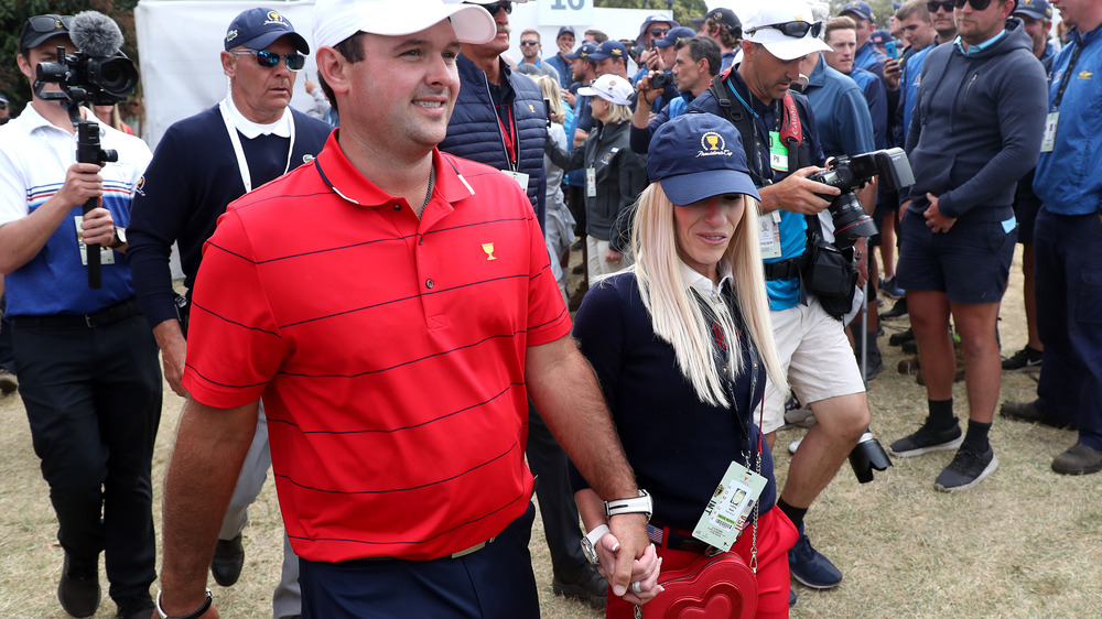 Patrick Reed and Justine Reed walking hand in hand, both wearing hats, surrounded by photographers and fans 