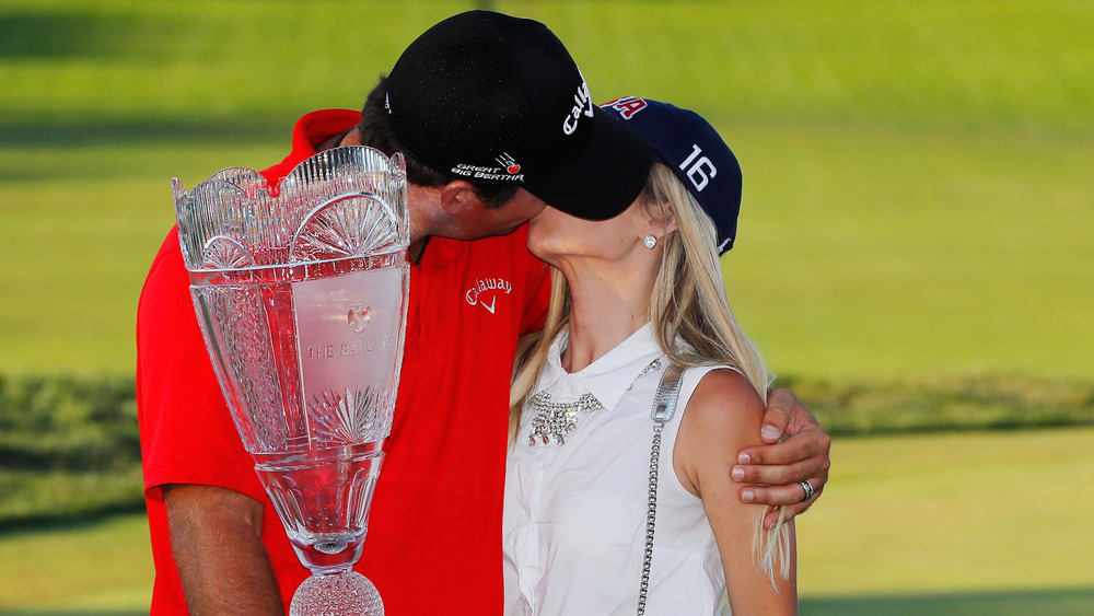 Patrick Reed and Justine Reed kissing, both wearing hats, on the golf course, wearing hats