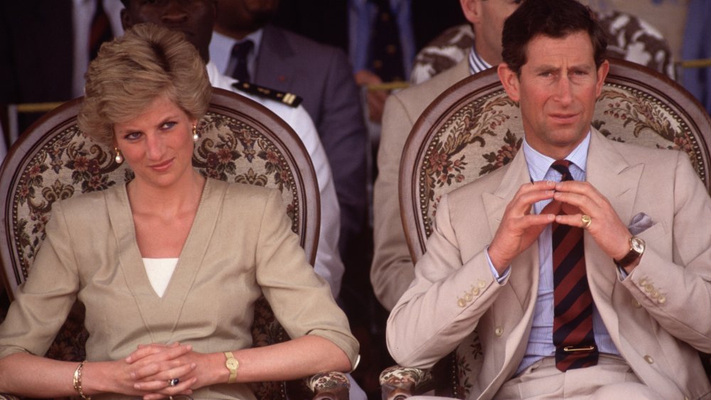 Princess Diana and Prince Charles, sitting next to each other in tan outfits, both with serious expressions
