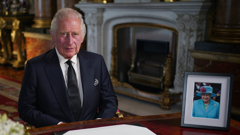 King Charles III sitting next to a photo of the queen