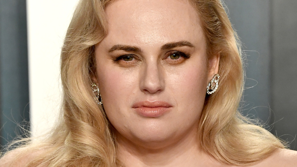 Rebel Wilson looking serious in a pink dress on the red carpet