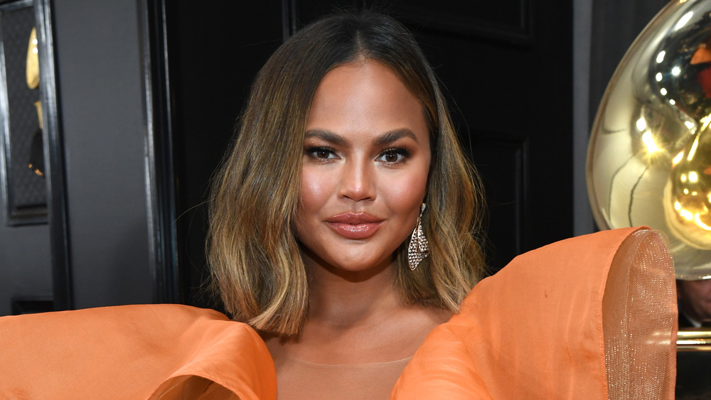 Chrissy Teigen wears an orange dress on the Grammy's red carpet