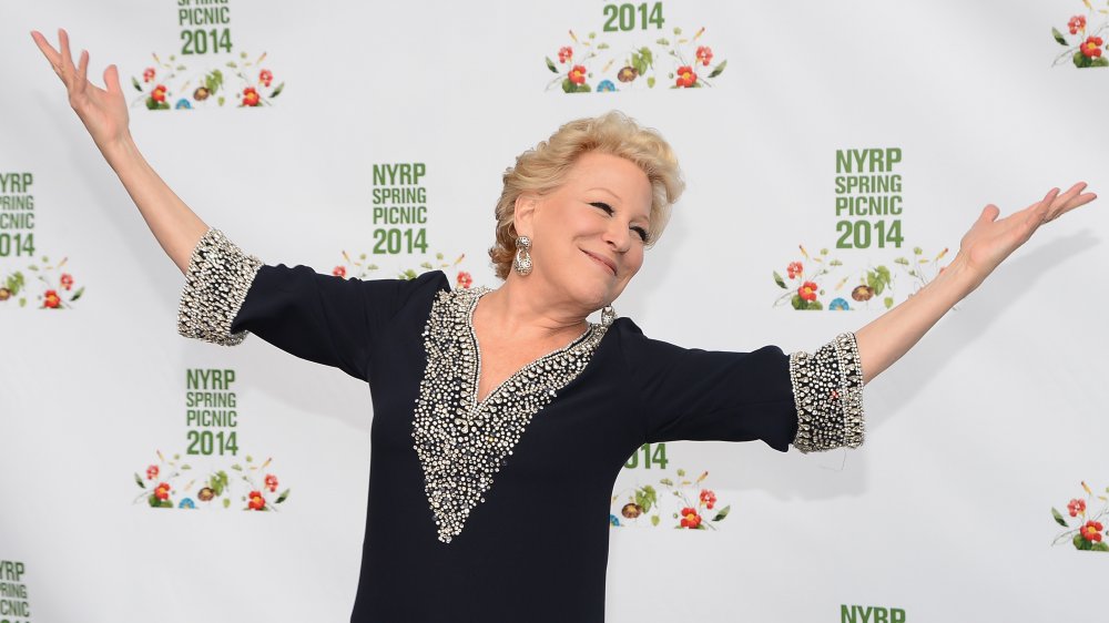 Bette Midler smirking with her hands up in the air on the red carpet