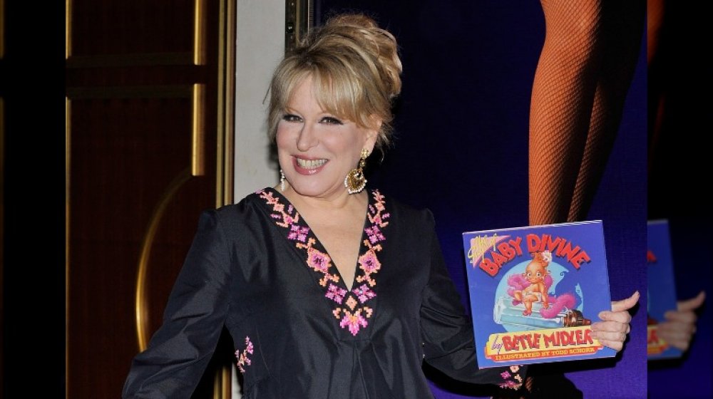 Bette Midler smiling while holding her Baby Divine book