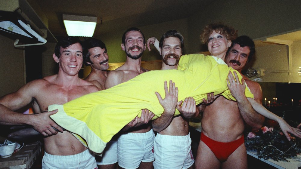 Bette Midler in a yellow dress being carried by a group of men